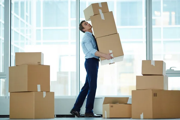 Young businessman carrying huge stack of big boxes with office supplies during relocation to modern business center