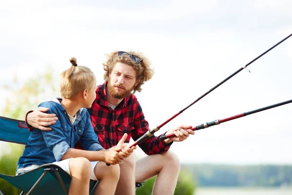 若い男と釣り竿湖のそばに座っていて 夏の週末の話と彼の息子 — ストック写真