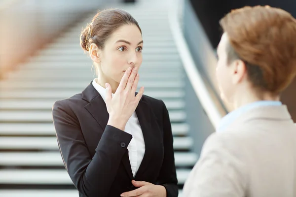 若い従業員の口に手のひらを維持し 彼女の同僚に話している間の驚きを表現します — ストック写真