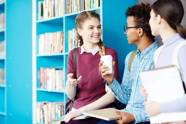 Três Estudantes Felizes Com Livros Conversando Durante Coffee Break Biblioteca — Fotografia de Stock
