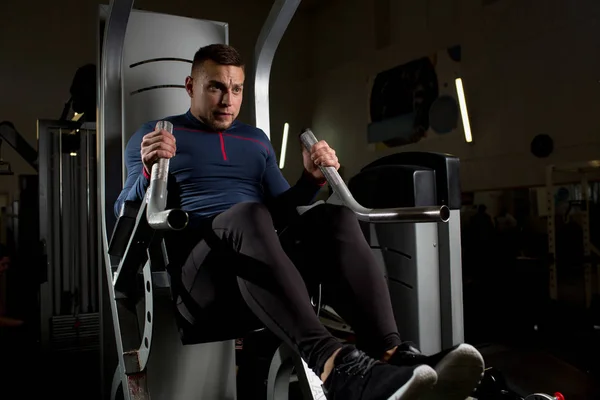 Sportlicher Junger Mann Sitzt Auf Trainingsgeräten Und Zieht Beim Training — Stockfoto