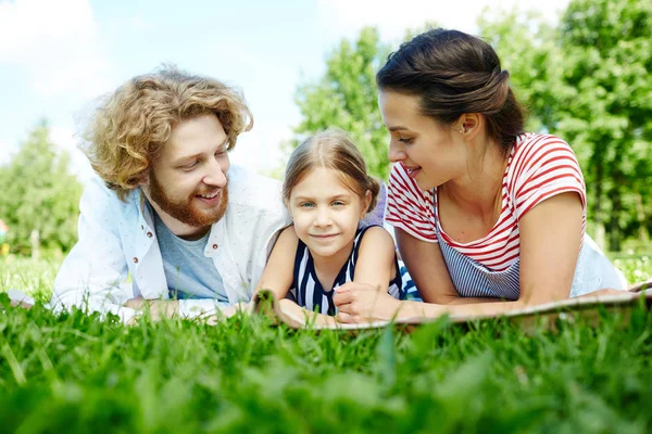 年轻的父亲和母亲看着他们的女儿 同时享受绿色草坪上的休闲 — 图库照片