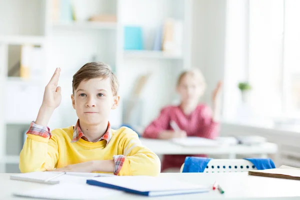 Selbstbewusster Sekundarschüler Mit Erhobener Hand Schreibtisch Sitzend Auf Dem Hintergrund — Stockfoto
