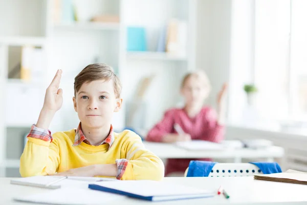 Självsäker Sekundära Skolpojke Med Upphöjda Handen Sitter Vid Sitt Skrivbord — Stockfoto