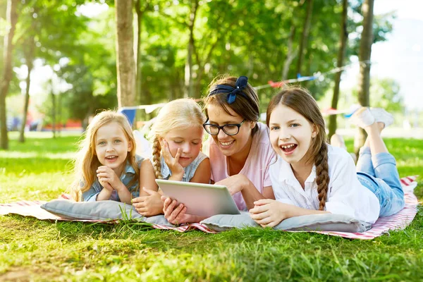 快乐的小女孩和他们的老师与平板电脑花费周末在公园通过观看电影或视频在网 — 图库照片