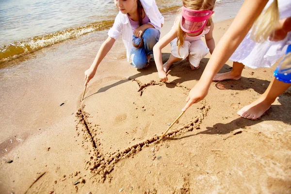 Drie Kleine Meisjes Met Stokken Tekening Hart Zand Door Waterside — Stockfoto