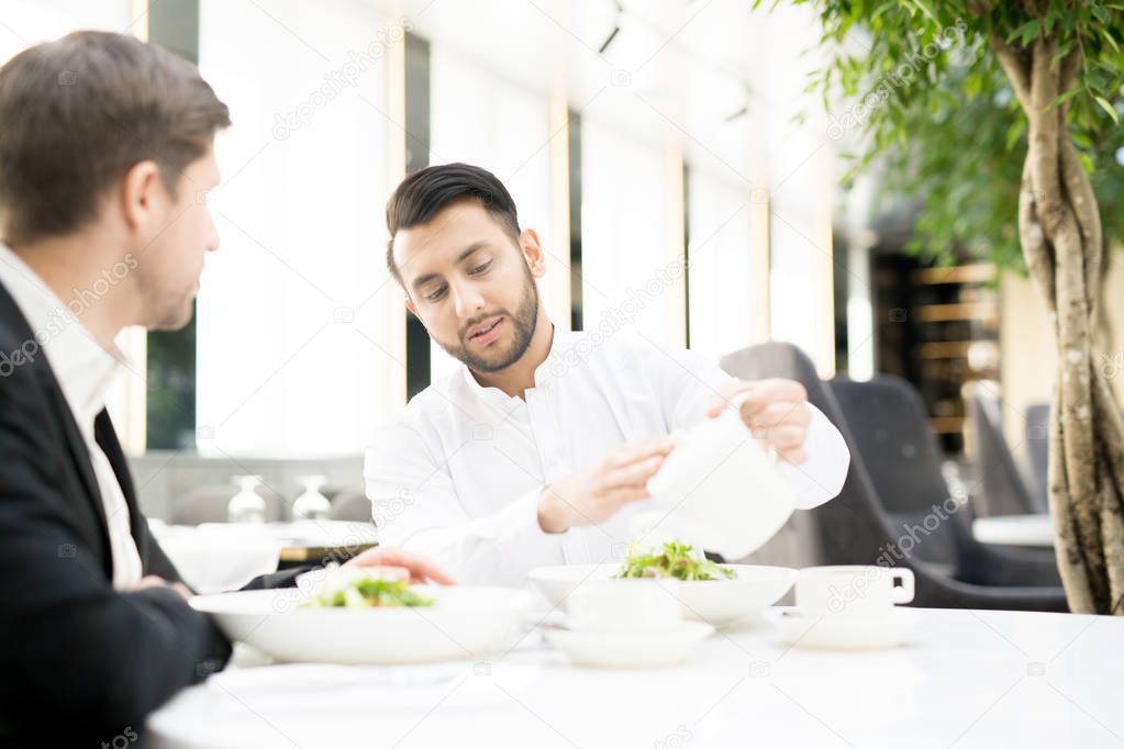 Young man adding some hot water into his cup of tea during business lunch with colleague in restaurant