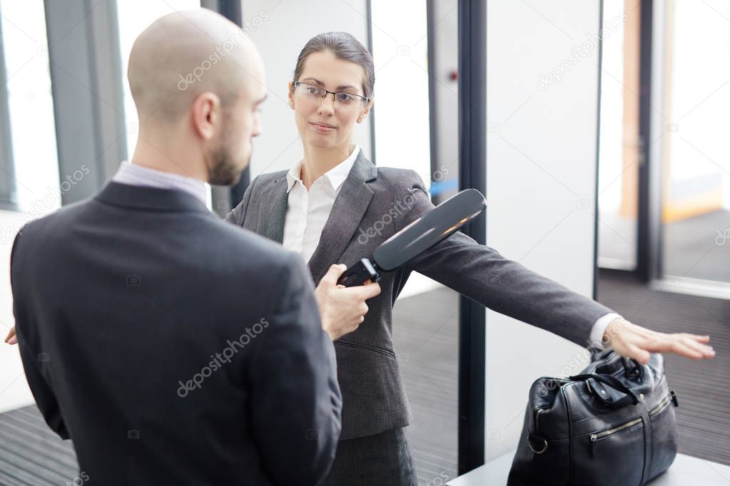 Contemporary security guard with metal detector checking one of passengers on entrance of airport