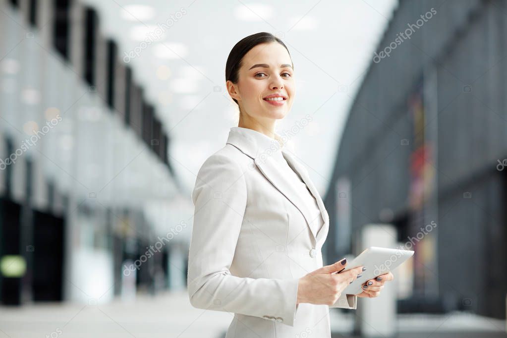 Young female manager with touchpad standing in the middle of airport lounge while looking for some information in the net