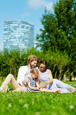 Dokunmatik yüzey ve Park yeşil çim ve net film seyrederken oturan ailesi ile küçük kız