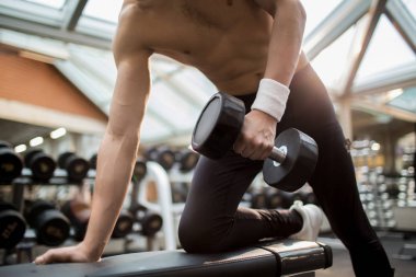 Gömleksiz adam ağır dumbbell sağ kolu ve bacağı yaslanmış iken onun kol kasları eğitim ile