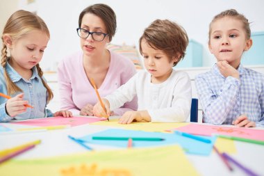 Üç sevimli çocukla tarafından masanın ve ilkokulda boya kalemi ile çizmek için öğrenme öğretmen