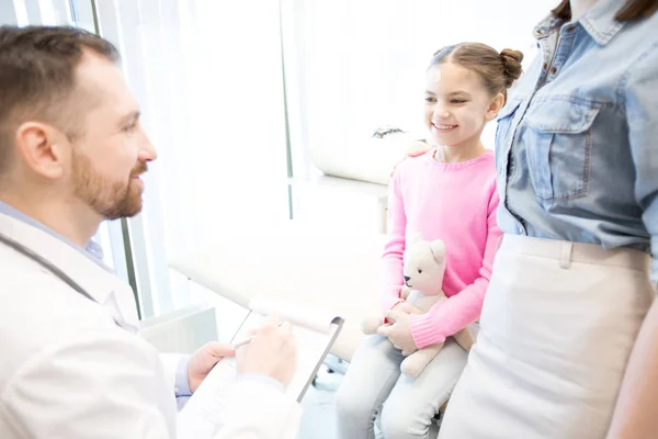 愉快的女孩与 Teddybear 和她的母亲谈话与医生 当参观现代诊所时 — 图库照片