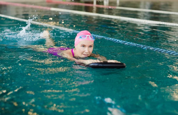 シニア女性の黒いゴム製のリングで押しながら前方のプールで水泳水着 — ストック写真