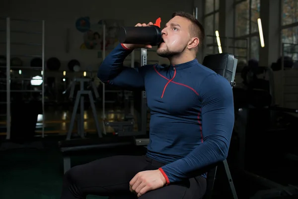 疲倦的肌肉运动员从塑料杯子喝水在锻炼之间在健身房 — 图库照片