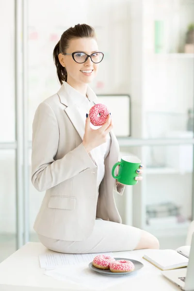 ドーナツと彼女の机の上や オフィスでおやつを持つホット コーヒー一杯で幸せな若い女性 — ストック写真