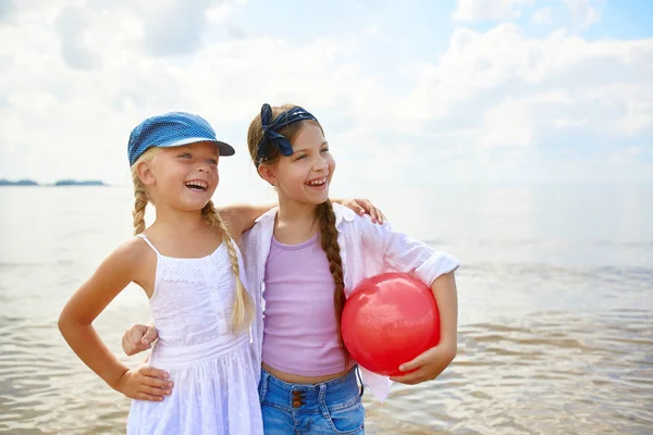 Две Смеющиеся Девушки Красным Мячом Стоят Песчаном Пляже Проводя Выходные — стоковое фото