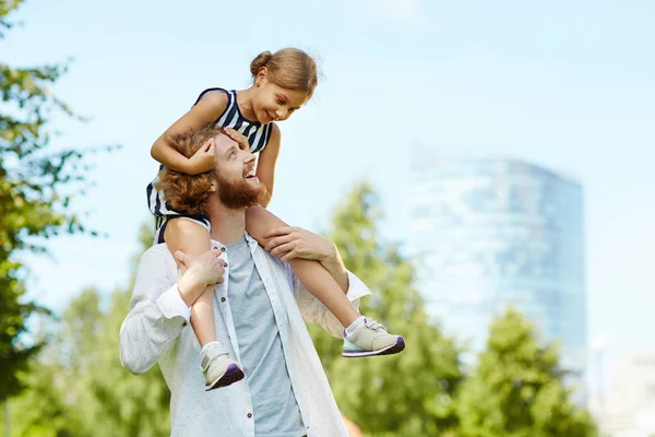 年轻的父亲抱着他的小女儿在肩上和她说话时 在公园散步 — 图库照片