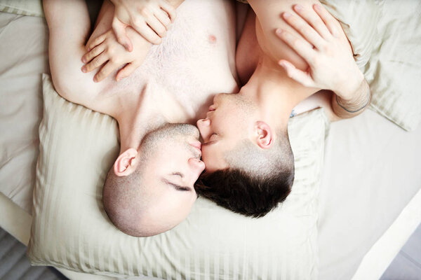 Overview of amorous guys lying on pillow while sleeping in embrace