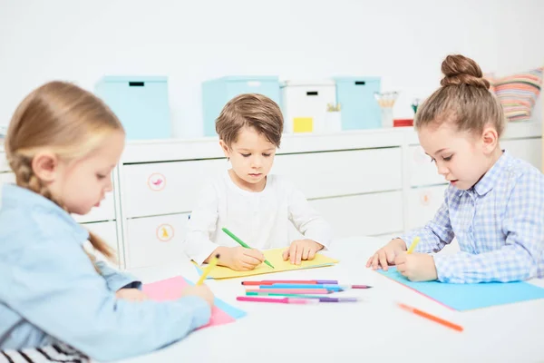 一群三小朋友坐在幼儿园里 用蜡笔一起画画 — 图库照片