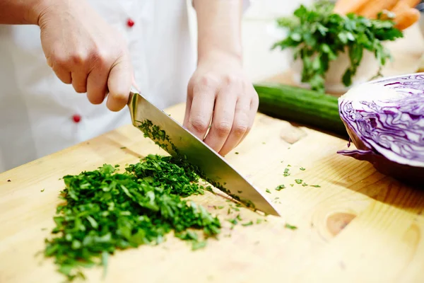 手用锋利的钢刀切碎绿欧芹叶子在木板上做沙拉或炖菜 — 图库照片