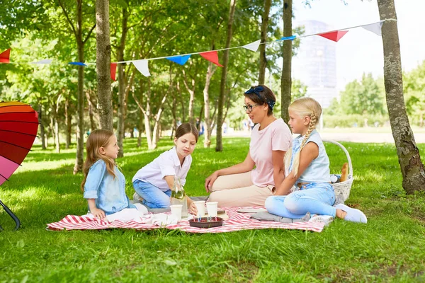 人の女の子と遊び場からそれほど遠くない公共の公園で緑の芝生のピクニックを持つ若い女性 — ストック写真