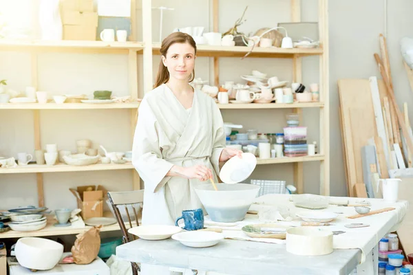 El sanatları stüdyosunda çalışırken özel plastik kabın içinde sıvı kil karıştırma plaka ile genç kadın