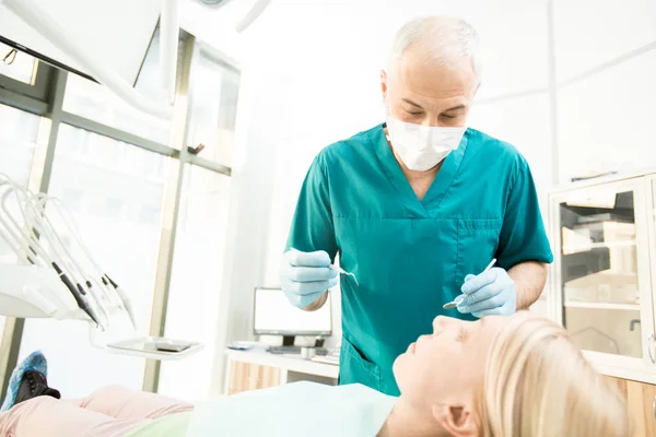 专业牙医在制服倾斜在他的患者之前检查与仪器 — 图库照片