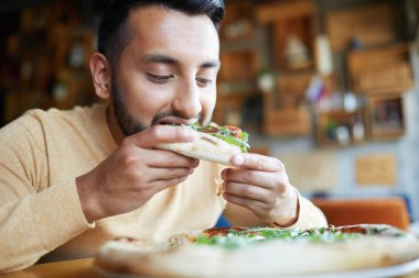 Kafede masa başında otururken iştah açıcı pizza dilim ısırma Aç adam