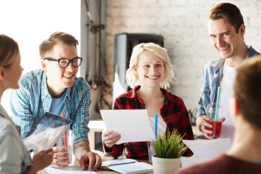 Modern ofiste ki toplantıda başlangıç projesi üzerinde işbirliği yapan fikirleri tartışırken neşeyle gülümseyen yaratıcı iş profesyonellerinden oluşan ekip