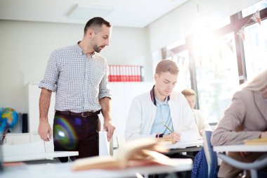 Sınıfta bireysel çalışma sırasında öğrenci notlarından birine bakan ciddi öğretmen