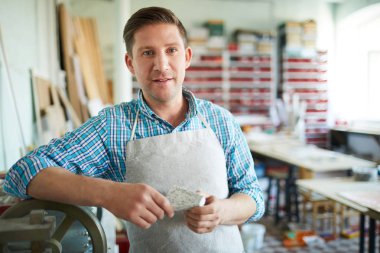 Mozaik sanatının modern stüdyosunda çalışırken sana bakan önlüklü genç adam.