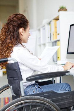 Ofiste bilgisayar önünde otururken tekerlekli sandalye okuma kağıdı meşgul genç yönetici