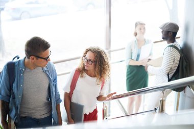 Sıradan giyimli genç bir çift merdivenlerde yürüyor ve derse giderken sohbet ediyorlar.