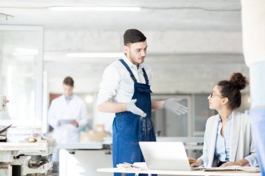 Eldiven ve tulumlu genç bir mühendis, meslektaşıyla konuşuyor.