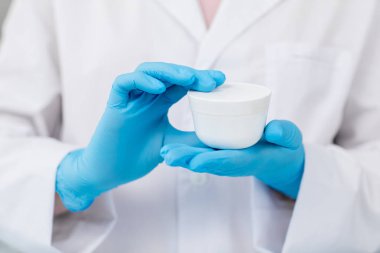 Yüz kremi ile beyaz plastik kavanoz tutan modern kozmetik eldivenli eller