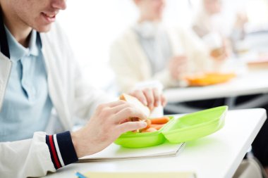 Çağdaş öğrenci plastik kap sandviç alarak ve masa başında yemek için gidiyor