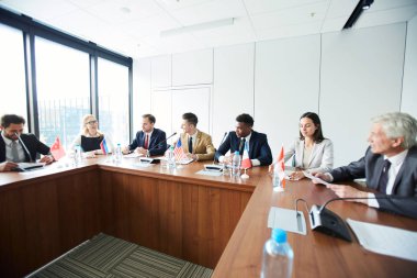 Toplantıda uluslararası tartışmalara katılırken gelecek planları tartışırken formalwear neşeli kendinden emin çok ırklı konsoloslar
