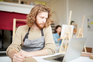 Akıllı öğrenci, masa başında otururken ve not defterinde çalışma notları yaparken çevrimiçi verileri okurken