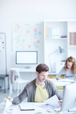 Genç ekonomist işyerinde otururken kağıtlarla ilgili mali verileri karşılaştırıyor