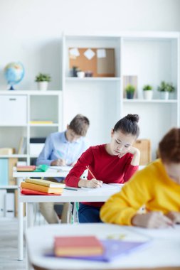 Çalışkan kız öğrenci sınıf arkadaşları arasında masa başında otururken copybook notlar yapma