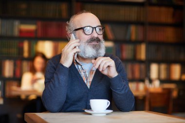 Kafede masasının dinlenirken smartphone ile konuşurken gri sakallı yaşlı adam