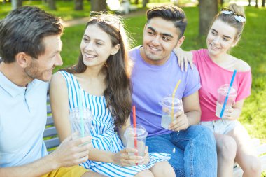 Sevecen ve mutlu gençler içki içiyor ve yaz günü açık havada konuşuyor