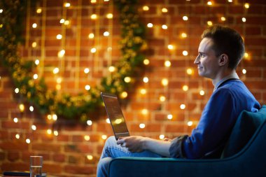 Mutlu yazılım köpüklü ışıklar ve iğne yapraklı çelenk ile Noel için dekore ofiste oturan dizüstü bilgisayar ile geliştiren