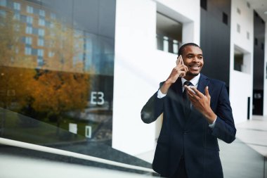 Mutlu genç Afrikalı işadamı takım elbiseli kentsel ortamda akıllı telefon ile konuşuyor