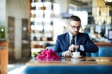 Şık adam kahve sahip restoranda masada otururken, seyretmek bakarak ve kız arkadaşı bekliyor
