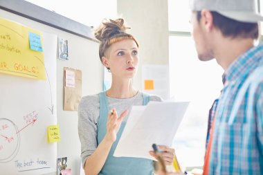 Hipster saç modeli ile ciddi girişimci kadın pazarlamacılar ofiste meslektaşı ile pazar analizi tutarken veri ve gesturing el açıklayan