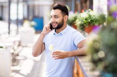 Açık terasta bar sayacına yaslanmış telefonla konuşan yakışıklı Orta Doğulu adamın bel kadar portre, kopya alanı