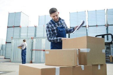 Taşımadan önce yük sepetinde paketlenmiş kutuların güvenliğini kontrol eden iş kıyafetindeki yükleyici adam