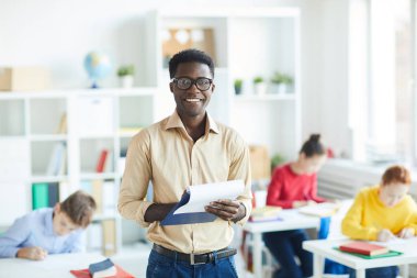 Neşeli ortaokul öğretmeni arkasında okul çocukları grubu ile kamera önünde duran belge ile